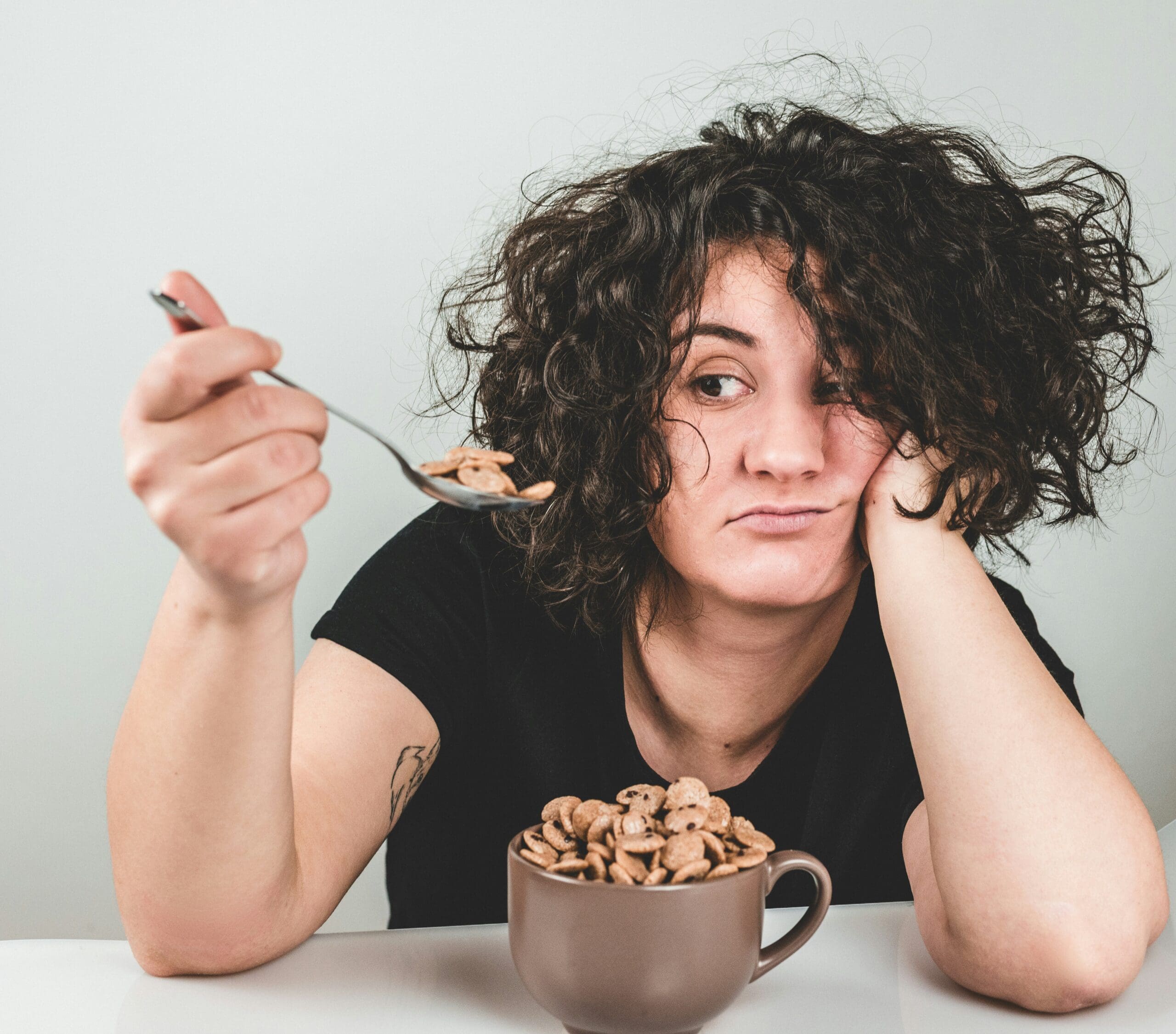 emotional eating concept with woman holding spoon and cereal looking frustrated or stressed