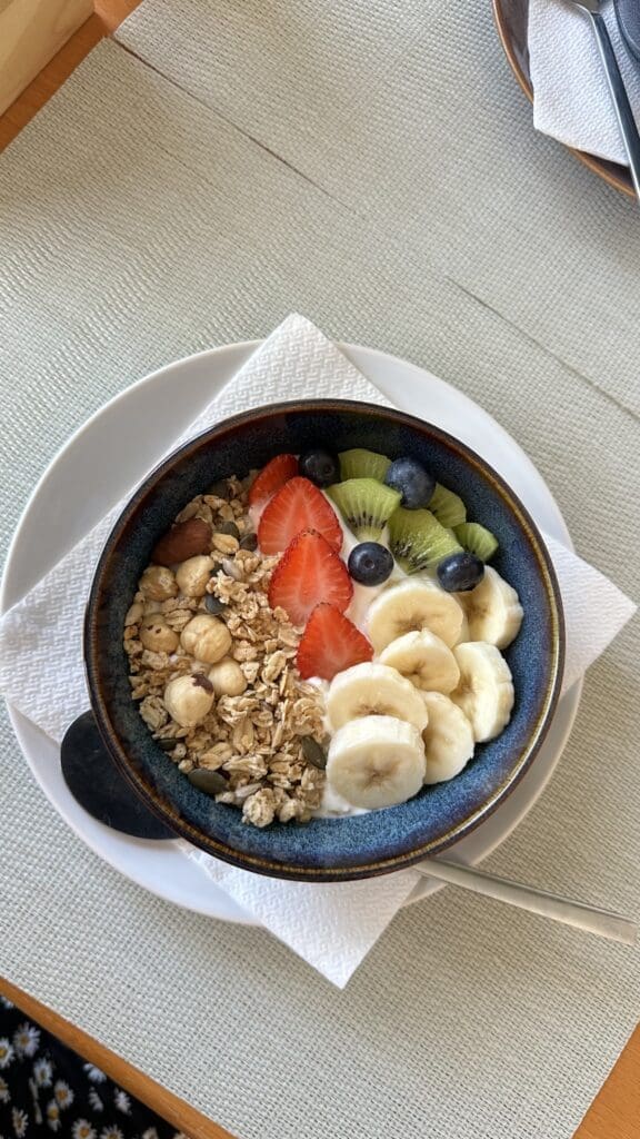 High protein oatmeal breakfast bowl topped with Greek yogurt, bananas, strawberries, blueberries, kiwi, granola, walnuts, and seeds for weight loss and appetite control.